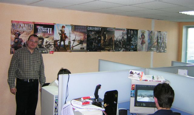 Vadim Khrulev, founder of KraiSoft, standing in the company's first office, with computers in front of him and a wall covered with game posters behind him